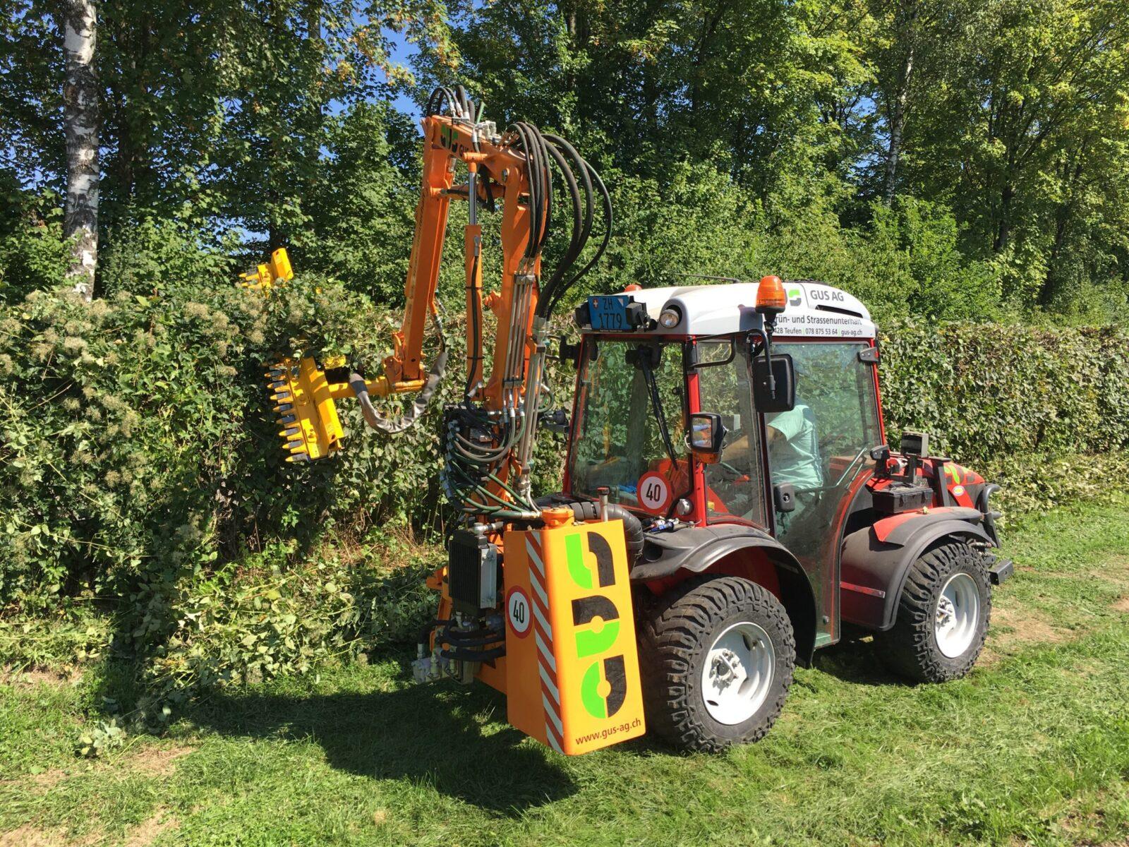 Kleiner Carraro Traktor mit Heckenschere und Fahrer beim Heckenschneiden.