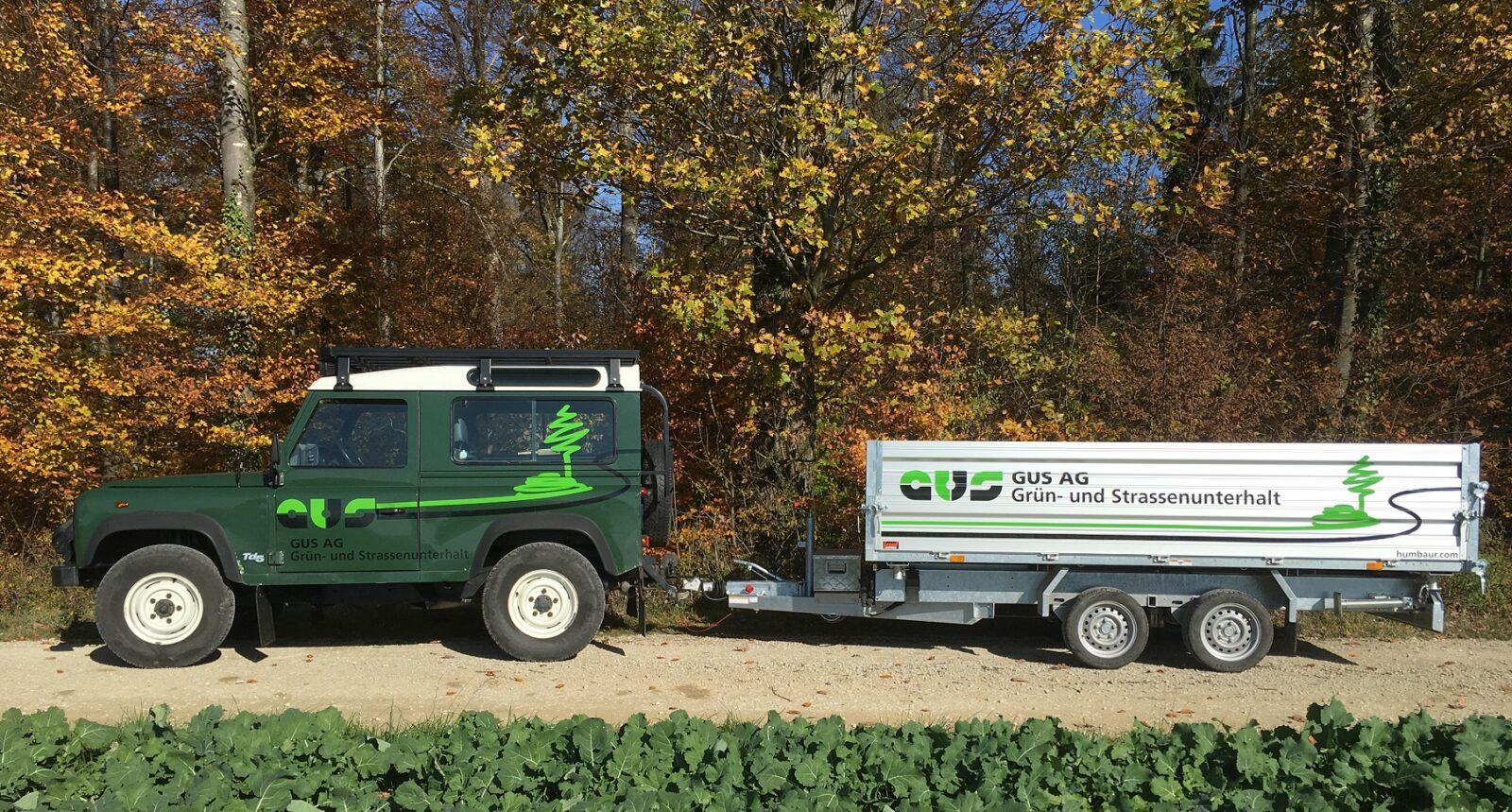 Grüner Landrover mit GUS-Logo und Anhänger.