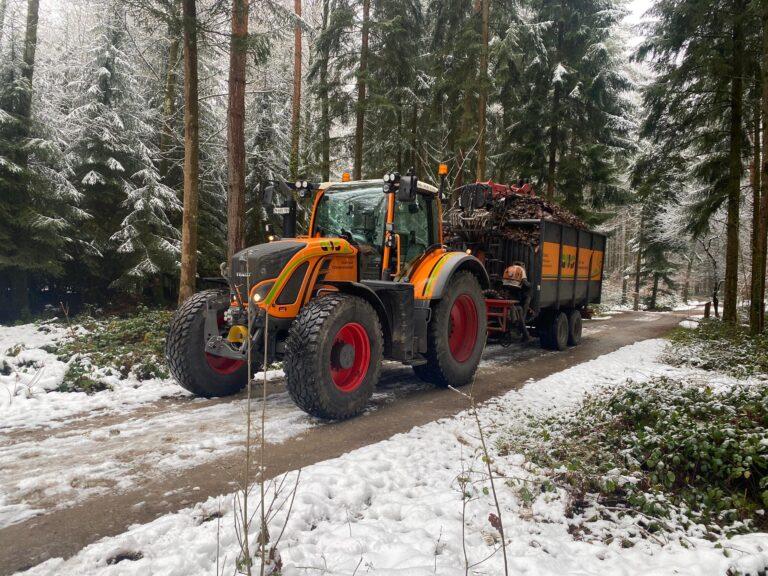 Fendt 720 mit Kranwagen und beladenem Anhänger im winterlich verschneiten Wald.