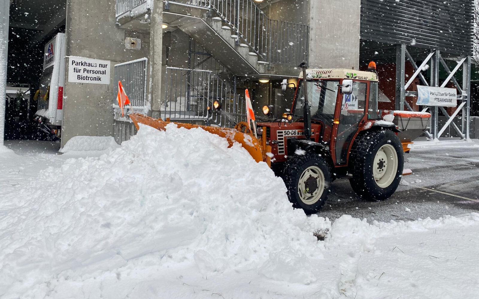 Der Traktor mit Pfadschlitten räumt den Schnee auf einem Industriegelände.